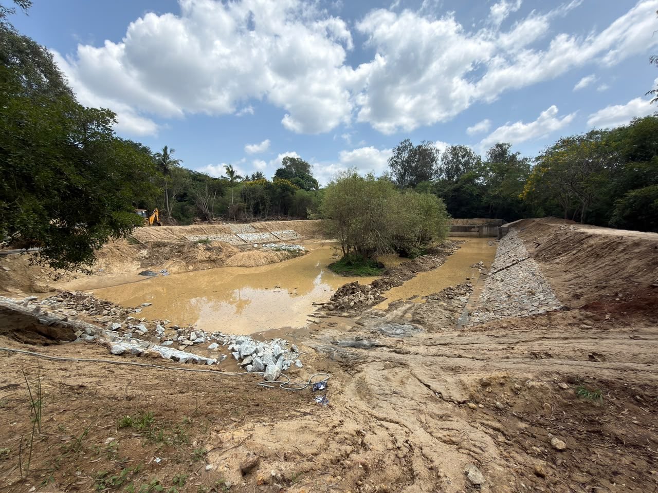 Wide view of the lake bed with stone pitching on the bank and an excavator in the distance